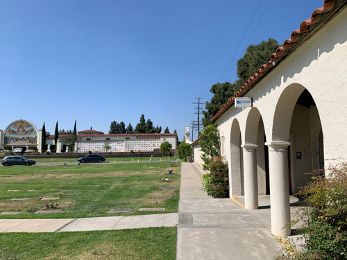 ["Restroom" sign on a colonnaded
pavilion; beyond a lawn with graves, the great mausoleum.]